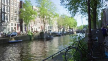Amsterdam kanal sahnesi bulanık odaklı, odakları kesilmiş bisikletler, klasik mimari, ve Hollanda 'nın göbeğinde parlak güneş ışığı altında yemyeşil.