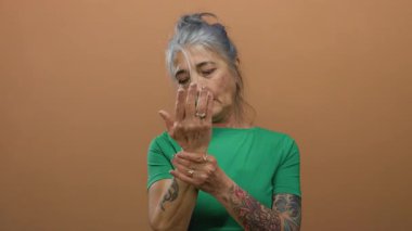 Yeşil tişörtlü, gri saçlı yaşlı kadın ellerini izole edilmiş kahverengi arka plan duvarına doğru inceliyor..