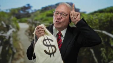 Takım elbiseli kıdemli bir adam parkta dolar sembollü para çantası tutuyor, açık havada yolsuzluk ve zenginlik öneriyor..