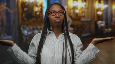 Müzede gözlüklü bir kadın, sanat ve heykellerle süslenmiş, çizgili bir gömlek giymiş, güzel ve zarif bir görünüm sergiliyor..