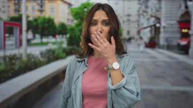 Şehir sokaklarında şaşkın bir ifadeyle genç bir İspanyol kadın, günlük kıyafetler giyiyor, şehir ortamında yüzünü ve duygularını vurguluyor..