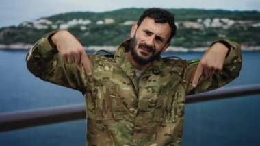 Sakallı, askeri üniformalı İspanyol bir adam okyanus ve arka planda yeşillik olan bir yolcu gemisini işaret ediyor..