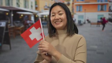 İsviçre bayrağını açık havada tutan genç bir kadın neşeli bir ifadeyle İsviçre 'de canlı bir sokakta seyahat ve kültürel gururu temsil ediyor..