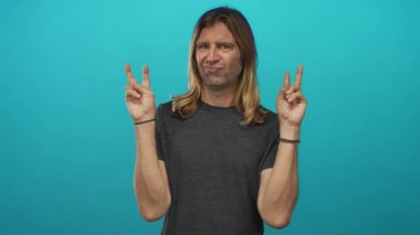 Uzun sarı saçlı bir adam iki eliyle parmak hareketleri yapıyor ve stüdyoda şüpheli bir ifade sergiliyor. Şüpheci mizah anlayışı..