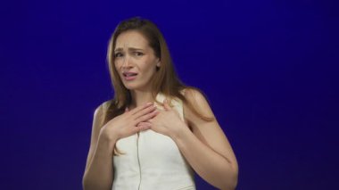 Mavi bir stüdyoda beyaz bir elbise giyen korkmuş yüz ifadesi olan beyaz bir kadın, korku..