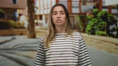 Şehir binaları ve arka planda palmiye ağaçları olan bir caddede hoşnutsuz görünen genç bir kadın..