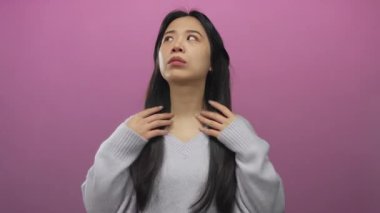 Kadın duygularını pembe arka plana karşı elleri ile ifade eder süveter giyer stüdyo ortamında uzun saçlarını göstererek samimi ve doğal anları yakalar.