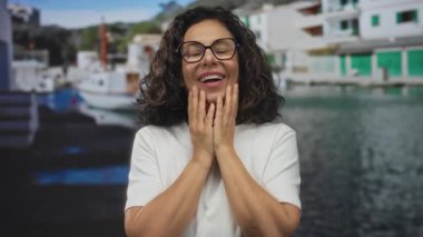 İspanyol kadın gözlüklü ve beyaz gömlekli. Deniz manzaralı bir limanda tekneler ve renkli binalarla eğleniyor ve şaşırıyor..