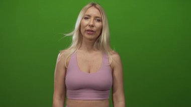 Sarışın beyaz kadın kollarını omuz hizasından yukarı kaldırır ve yeşil ekrandaki stüdyoda gözlerini kapatır..