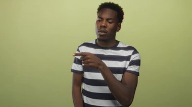 Çizgili gömlekli genç Afro-Amerikan adam yeşil stüdyodaki görünmeyen nesneyi işaret ediyor; belirsizlik belirsizliği.
