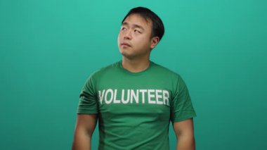 Yeşil gönüllü gömleği giyen genç adam, yeşil arka plana karşı düşünceli bir ifade sergiliyor..