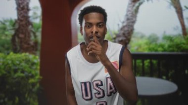 Genç Afrikalı Amerikalı adam bina sessizliği için parmaklarını dudaklarına tutar; sessizlik sükunet sükunet.