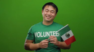 Meksika bayrağı taşıyan gülümseyen bir adam yeşil arka planda gönüllü tişört giyiyor neşeli genç izole edilmiş..