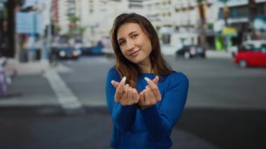 Kadın kalp sembolü yaparken parmakları açık havada, mavi kazak giymiş duygularını ifade ediyor..