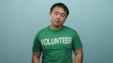 Mavi arka plan üzerine yeşil gönüllü tişörtü giyen Asyalı adam el hareketleriyle duyguları resmediyor.