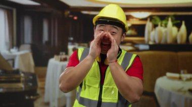 Güvenlik yeleği giyen ve sarı kasklı bir adam restoran ortamında neşeli bir şekilde bağırıyor. Beklenmedik bir şekilde inşaat atmosferiyle günlük yemekleri harmanlıyor..