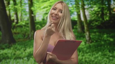 Kadın panoya yazıyor ve kalemi ormandaki yemyeşil kanopi ile birlikte sayfanın üstünde tutuyor; yoğunlaşma odaklama organizasyonu.