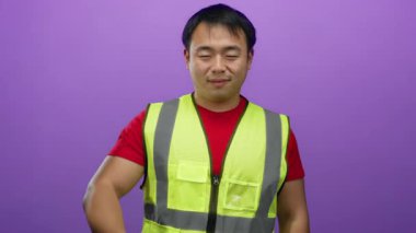 Güvenli bir yelek giyen genç adam canlı mor bir arka plana karşı neşeyle poz veriyor, pozitiflik ve ulaşılabilirlik taşıyor..