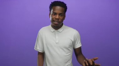 Mor stüdyoda el kol hareketi yaparken gelişigüzel gülümseyen Afrikalı Amerikalı bir adam..