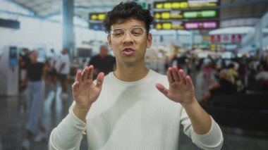 Gözlüklü genç İspanyol, avuç içini tutarak havaalanı terminalinde sakin bir jest yapıyor..
