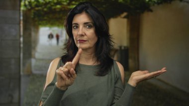 Kadın sokakta ciddi yüz ve parmak gösterme ve açık avuç hareketi gösteriyor..