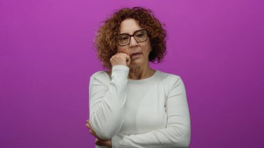 Çenesi dinlenmiş bir kadın canlı pembe bir duvarın önünde düşünceli bir ifade takınıyor.