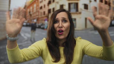 Woman gesturing passionately on bustling street showing her vibrant personality and expressive emotion while surrounded by urban scenery and lively atmosphere.