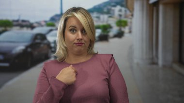 Kadın açık havada caddede ince baş eğik ve büzüşmüş dudaklarla solunu işaret ediyor..