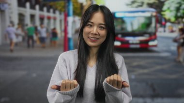 Kalabalık bir caddede el kol hareketi yapan genç bir kadın otobüsle arka planda yayalar ve şehir ortamında gündüz vakti....