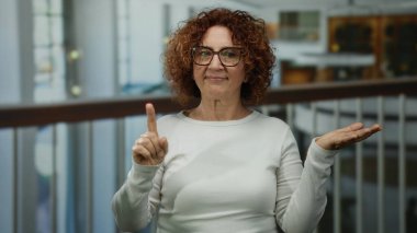 Otelde parmak ve avuç içi açık el kol hareketi yapan bir kadın, kapalı alanda belirsizlik olduğunu gösteriyor..