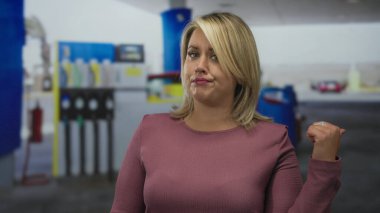 Pembe süveter giyen genç sarışın kadın kaşları çatık ve büzüşmüş dudaklarıyla pompayı işaret ediyor..