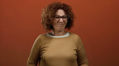 Kıvırcık saçlı İspanyol orta yaşlı kadın, kahverengi arka plandaki kötü kokuya garip bir yüz ifadesi veriyor..