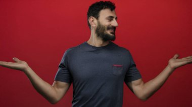 Sakallı İspanyol bir adam koyu kırmızı arka planda güvenle gülümsüyor günlük mavi gömlekler giyiyor ve elleri açık hareket ediyor..