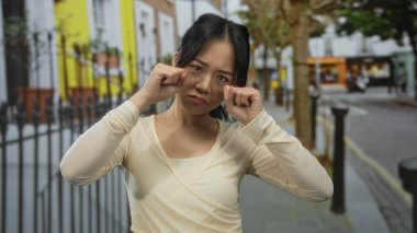 Sokaktaki genç Çinli kadın, açık havada jestlerle ağlayarak renkli bir arka planda, halk ortamında duygularını ifade ediyor..