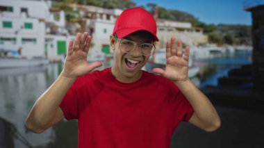 Kırmızı şapkalı ve gömlekli adam güneşli caddedeki limanda limandaki teknenin yanında elleri olan gözleri geniş bir gülümsemeyle kaplıyor..
