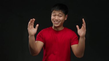 Kırmızı gömlekli genç adam, izole edilmiş siyah arkaplandan büyük jestler yapıyor. Coşku ve iletişim gösteriyor..