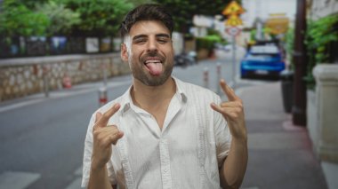 Meşgul caddede iki elle boynuz hareketi yaparken insan sırıtıyor ve dil gösteriyor..