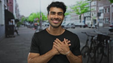 Sandık tutan ve park halindeki bisikletlerin ve bulanık binaların önünde gülümseyen Latin asıllı genç adam..