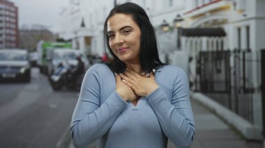 Canlı bir şehir sokak ortamında modern mimari ve açık gökyüzünün altında park edilmiş arabaların karışımıyla mutlu bir şekilde gülümseyen kadın..