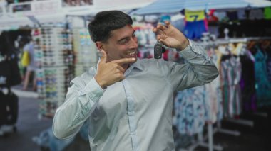 Arkasında renkli giyim mağazaları olan hareketli bir sokak pazarında araba anahtarı tutan ve yumruk sallayan adam; başarı sevinci.