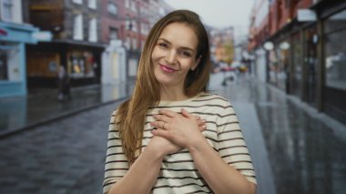 Arkadaki bulanık dükkanlarla ıslak şehir caddesinde duran sandık üzerinde el ele tutuşan genç beyaz kadın, minnettarlık..