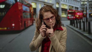 Şehir caddesinde akıllı telefondan konuşan bir kadın yoğun bir şehir ortamından geçen çift katlı otobüslerle modernlik ve geleneğin bir karışımını sergiliyor..
