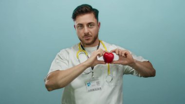 Steteskoplu doktor gibi giyinmiş sakallı genç adam, kırmızı kalbi mavi duvarın üstünde tutuyor..