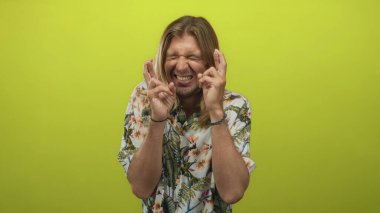 Çiçekli gömlek giyen uzun saçlı sarışın adam, parlak yeşil stüdyoda çıplak elleriyle çapraz parmaklar tutuyordu..