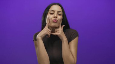 Kabarık yanaklı bir kadın canlı mor bir arka plana karşı neşeli poz veriyor, gençlik enerjisi ve cazibesi yayıyor, anlamlı hareketlerini vurguluyor..