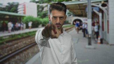 Çıtır beyaz gömlekli genç İspanyol adam kamerayı binanın önünde işaret ediyor..