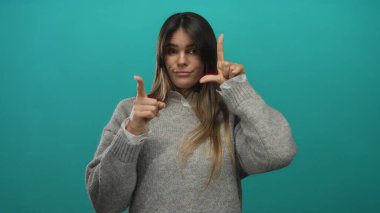 Süveter giyen İspanyol kadın yeşil arka planda ezikçe jest yapıyor. İğnelemeyi ya da mizahı simgeliyor.