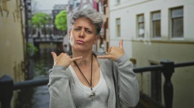 Gri kısa saçlı kadın nehir kanalı kenarında iki eliyle şehir caddesinde barış işareti yapıyor..