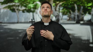 Şehir caddesinde karşıdan karşıya geçen adam siyah dini giysiler giymiş canlı yeşil doğa ve kentsel altyapının arasında umut ve inanç ifadesiyle yukarı bakıyor..