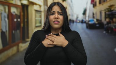 Yoğun bir caddede, göğsü göğsünde endişeli görünen bir kadın, şehir ortamında duygularını ifade ediyor..